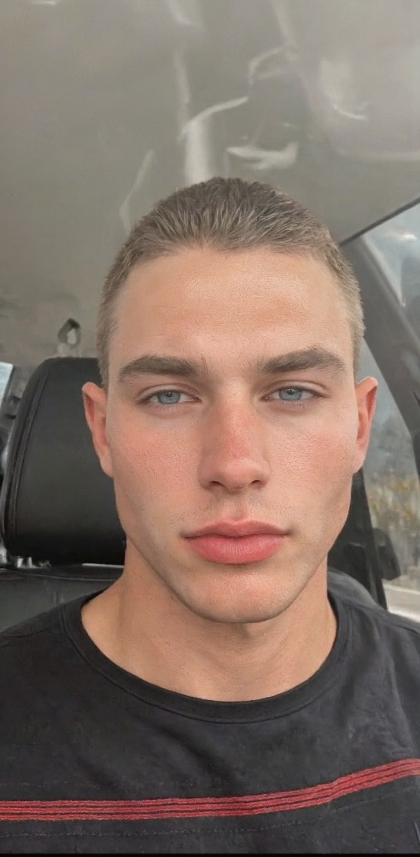 a close-up shot of a young man's face is seen in a car window. The man's eyes are a piercing blue,  and he has a serious e...