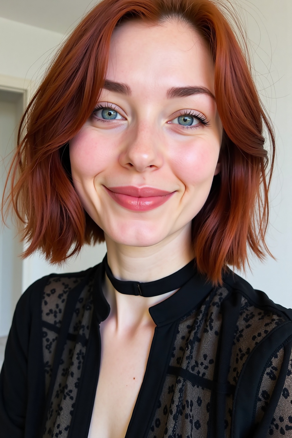 A close-up eye-level shot of a woman with reddish-brown hair and blue eyes. She is wearing a black lace shirt with a black...