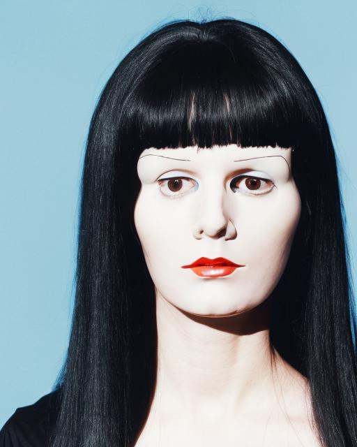 a woman with long black hair and a blue background is looking at the camera with a serious look on her face,  Daphne Allen...