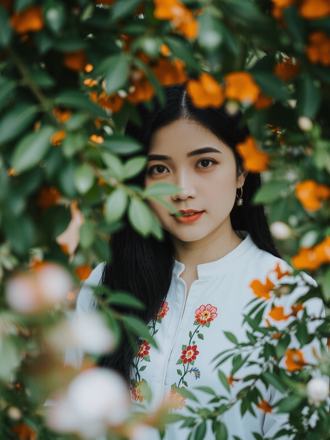 A woman stands amidst lush,  green foliage,  framed by vibrant orange and white flowers. Her dark hair contrasts with her...