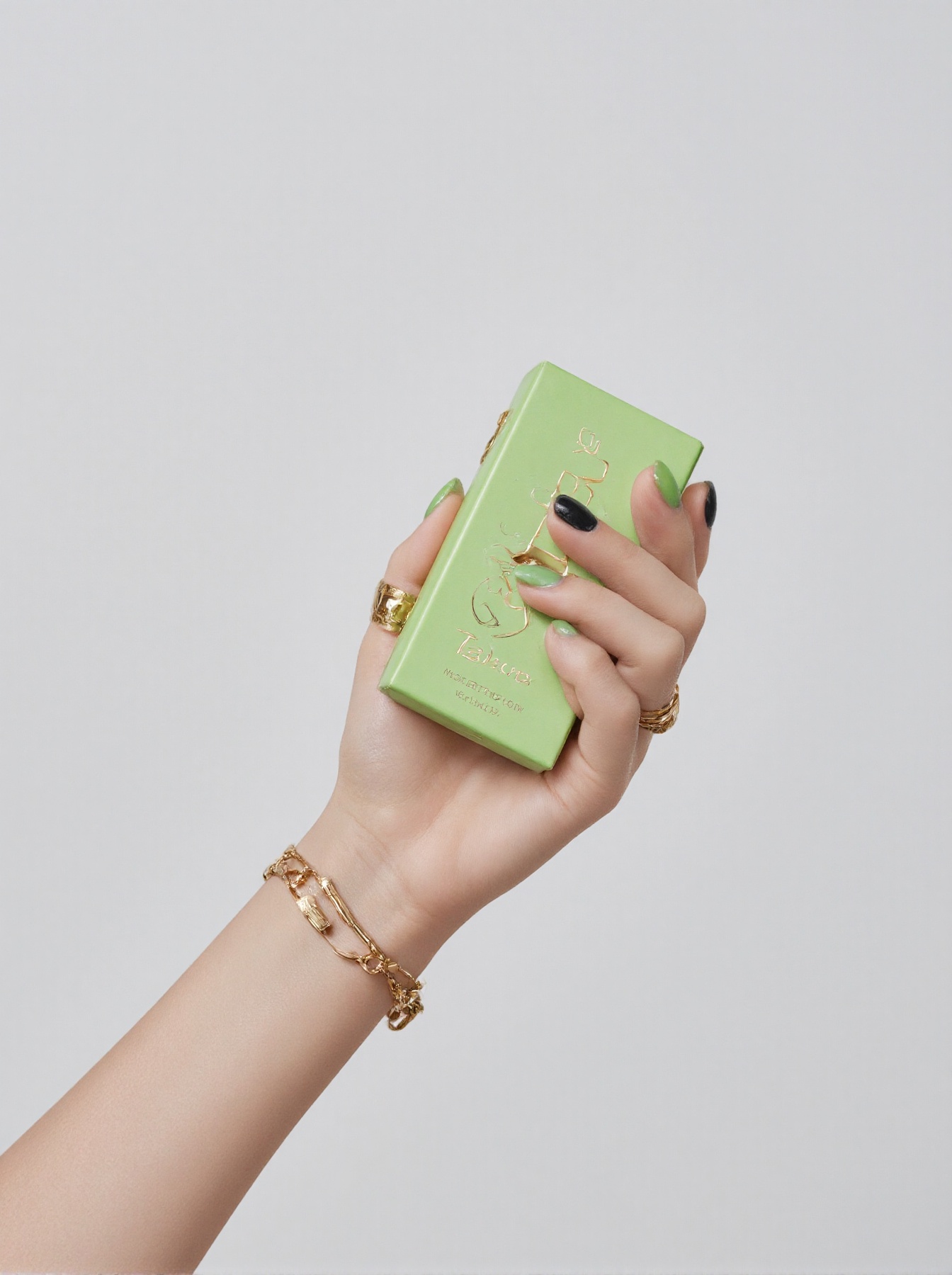 a woman's hand is adorned with a gold ring and a gold bracelet. Her fingernails are painted in a vibrant shade of green,...