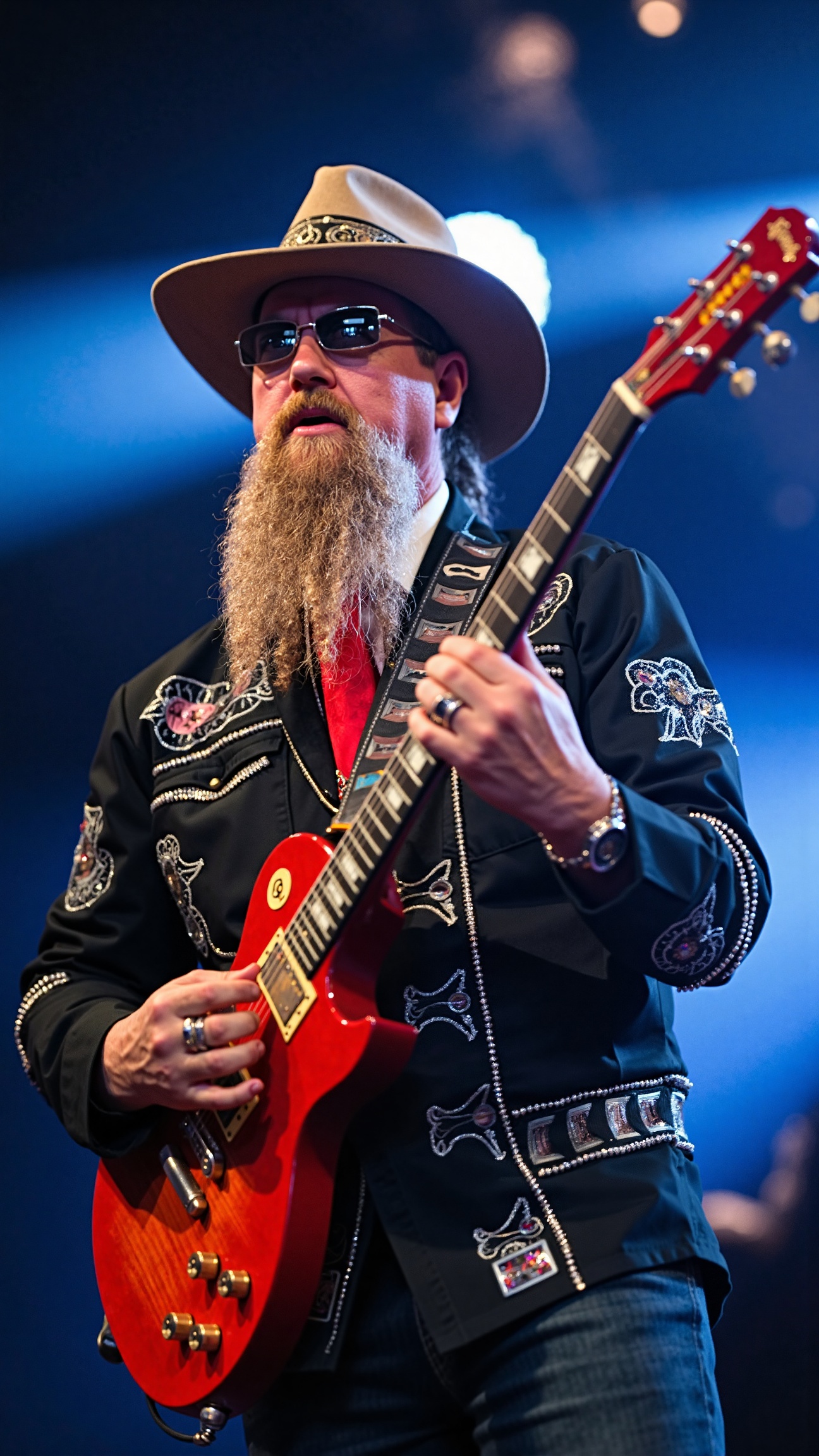 This is a high-resolution photograph of a male musician performing on stage. He is wearing a wide-brimmed hat with a banda...