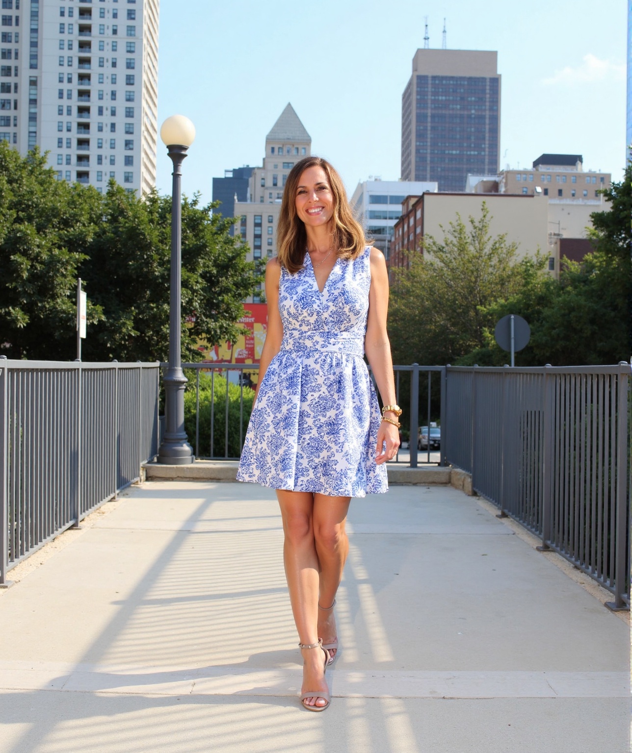 A woman stands confidently on a concrete pathway in an urban setting,  her sleeveless dress with blue and white floral pat...