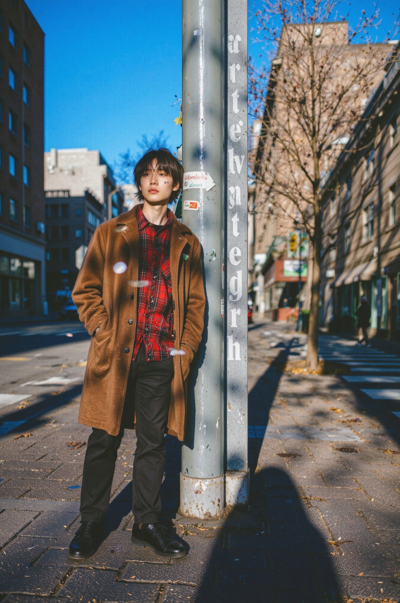a close-up of a subject standing casually against a pole in an urban setting,  wearing a brown coat over a red and black c...