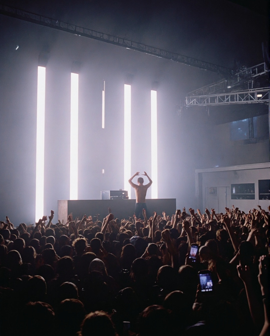 The image depicts a lively concert scene with a large crowd of people,  many of whom are raising their hands and cheering....