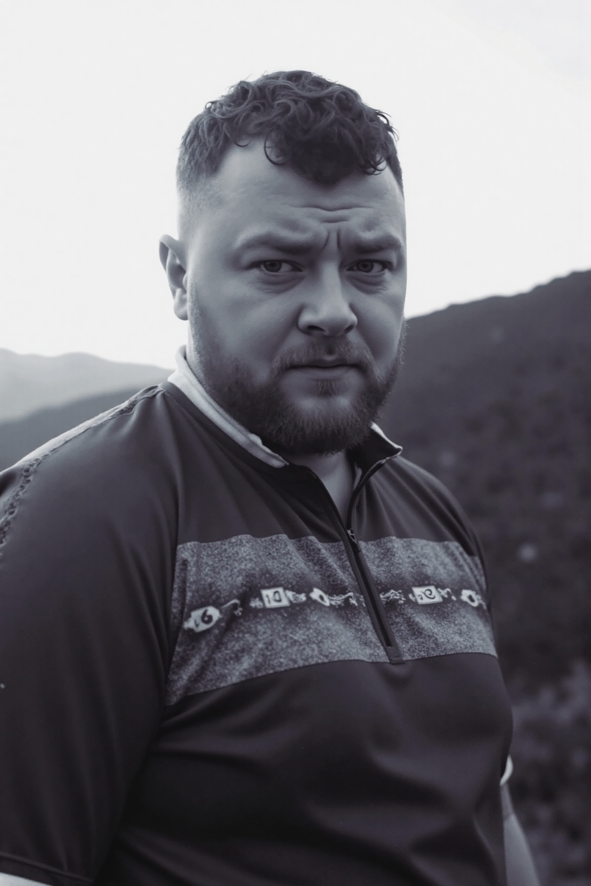 photo of jxr,  The image is a black-and-white photograph of a man with short hair and a beard,  wearing a patterned shirt...