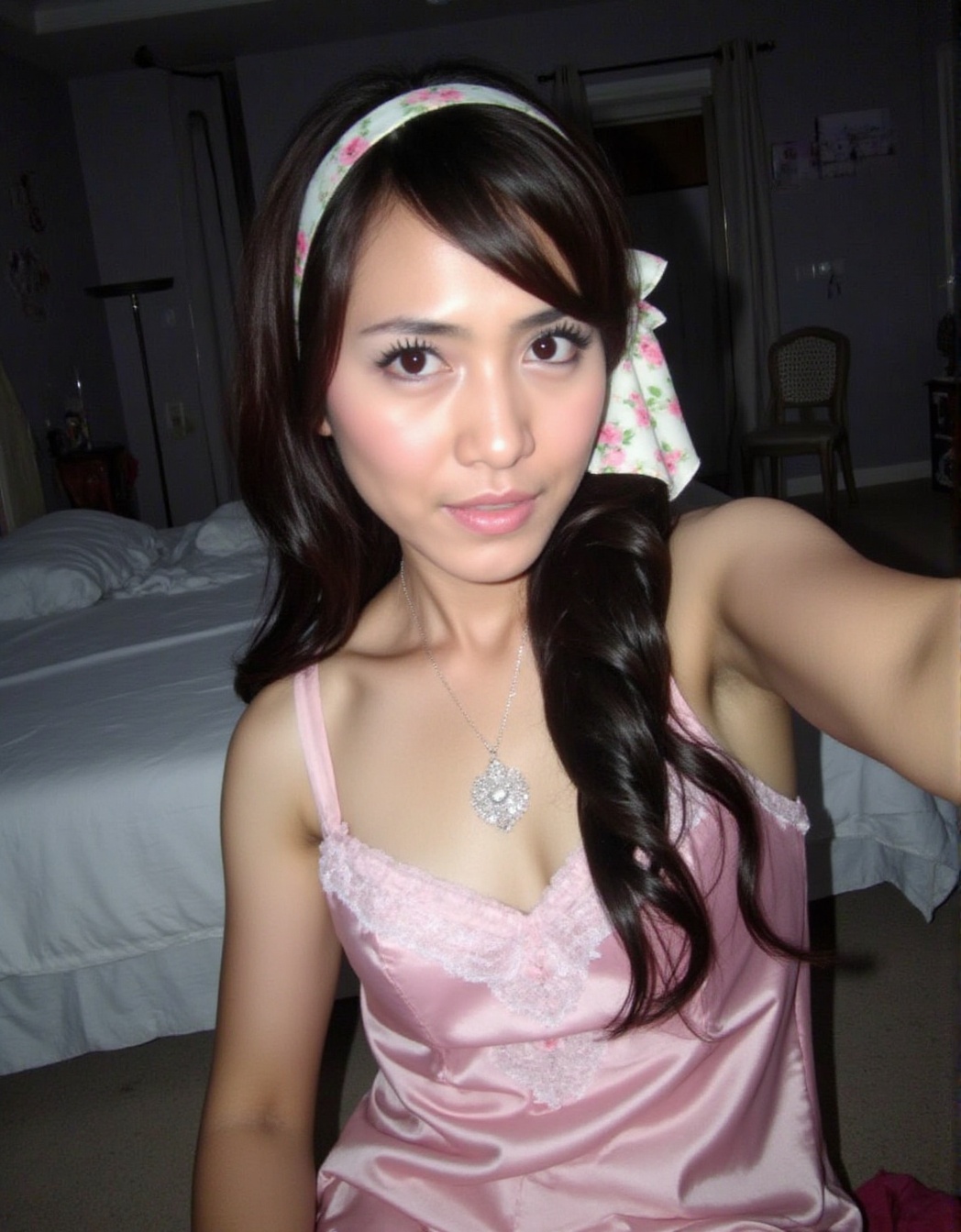 The image shows a person wearing a pink satin dress with lace detailing on the chest area. They have long,  wavy dark hair...