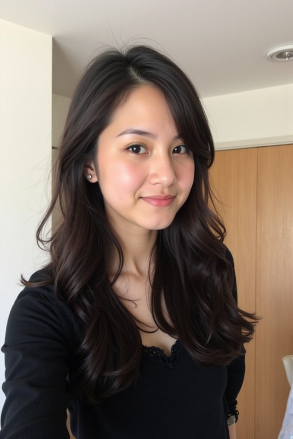 The image shows a young woman with long,  dark hair,  wearing a black top with a delicate lace trim. She is standing indoo...