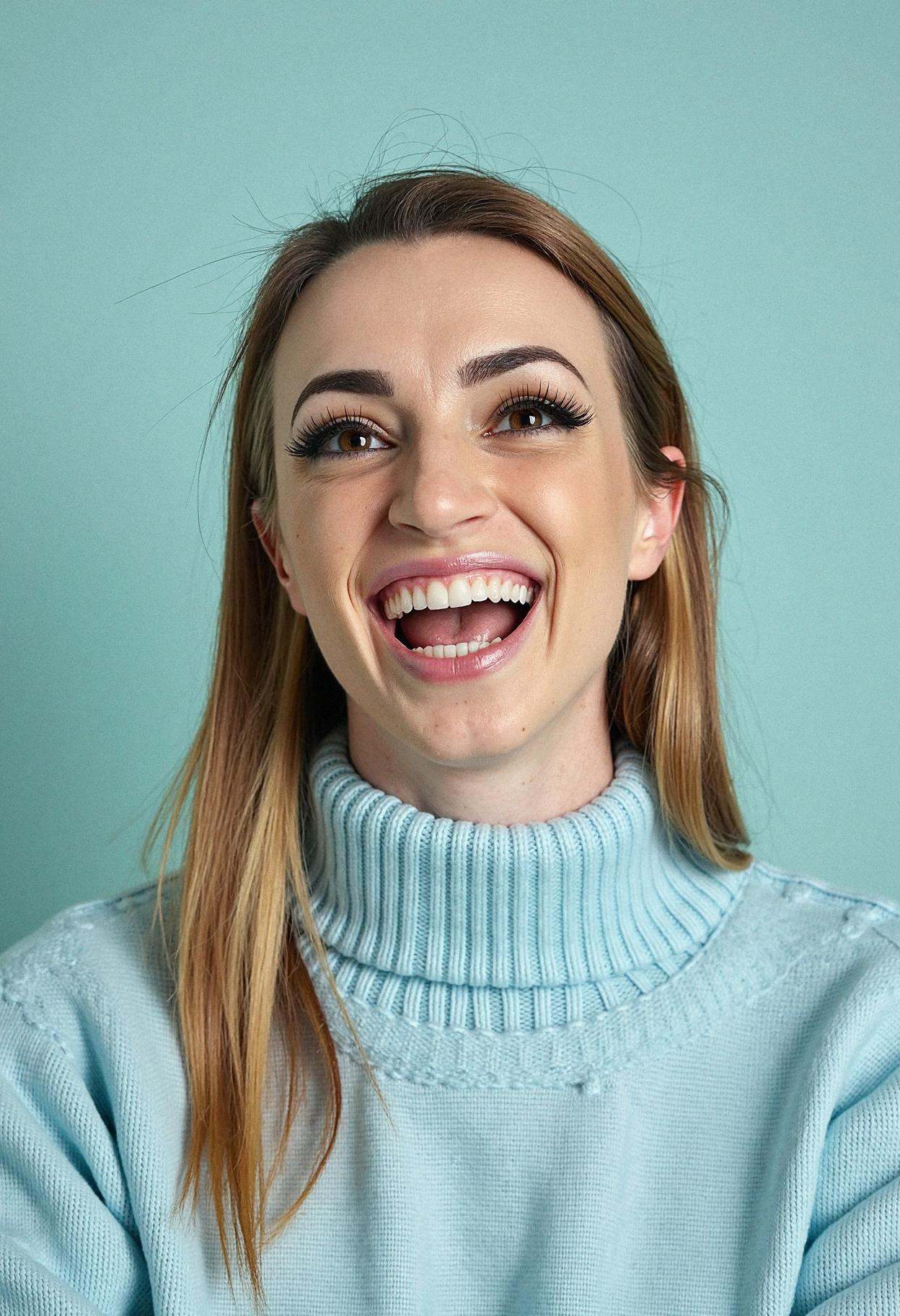 A professional head shot photograph of a woman letting out a light giggle,  situated against a solid pastel aqua backgroun...