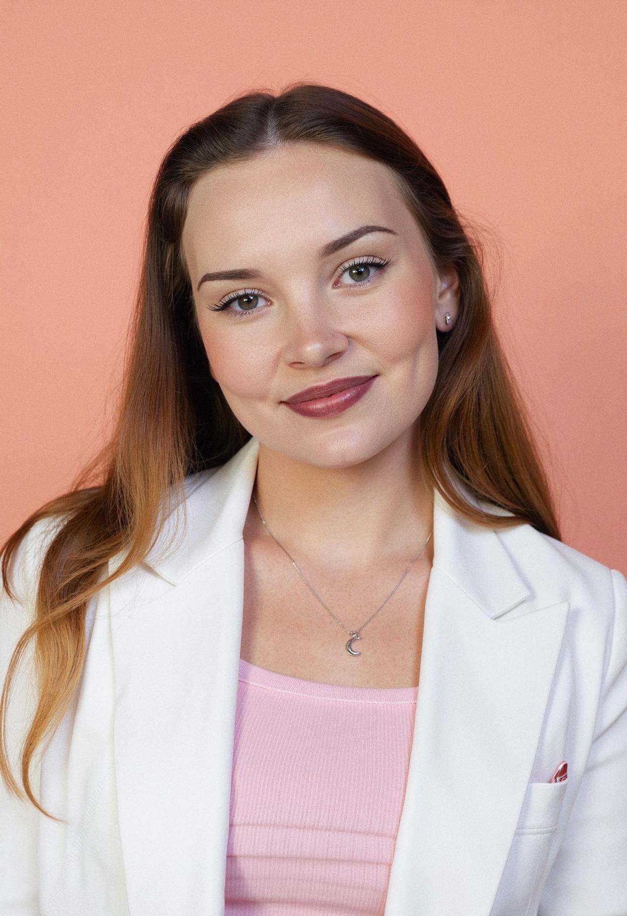 A professional head shot photograph of a woman with a warm smile,  captured against a solid gentle pastel peach background...