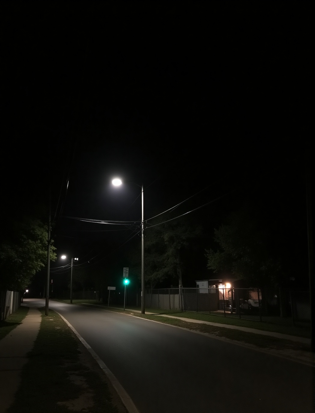 a quiet,  nighttime street scene. The road is illuminated by streetlights,  casting a soft glow on the pavement. On the le...