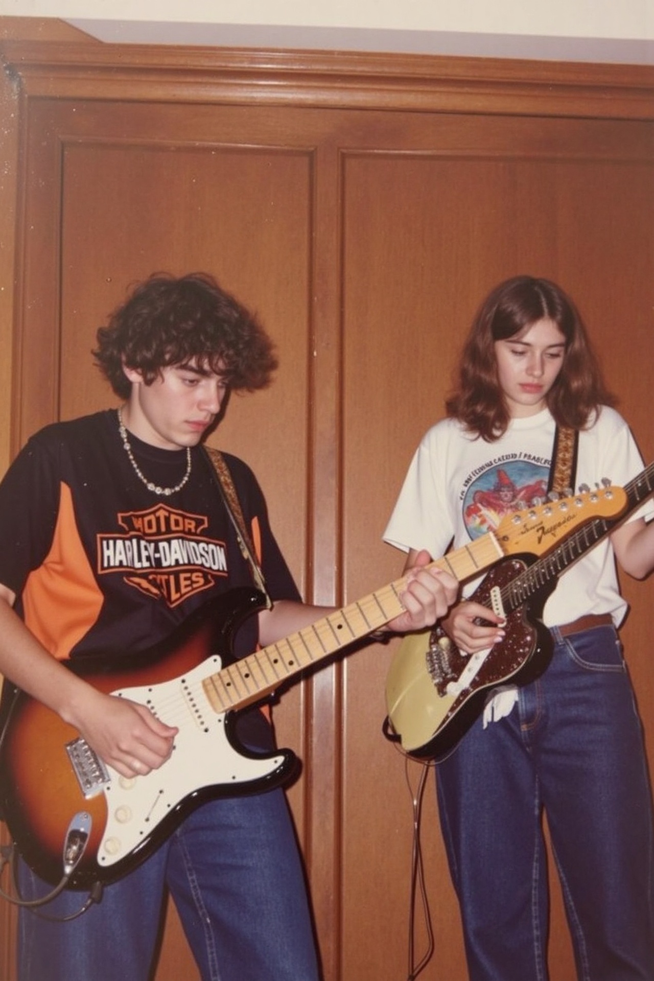 A photograph of two young person playing electric guitars indoors. The man on the left has curly brown hair wears a black...