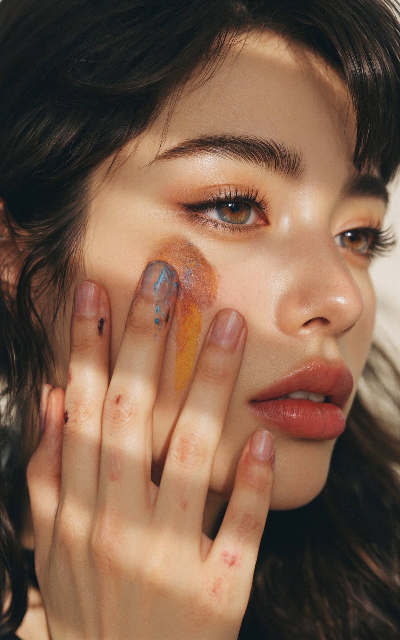 A closeup portrait of a young artist with a smudge of charcoal on her cheek and a thoughtful expression. Her fingers,  lig...
