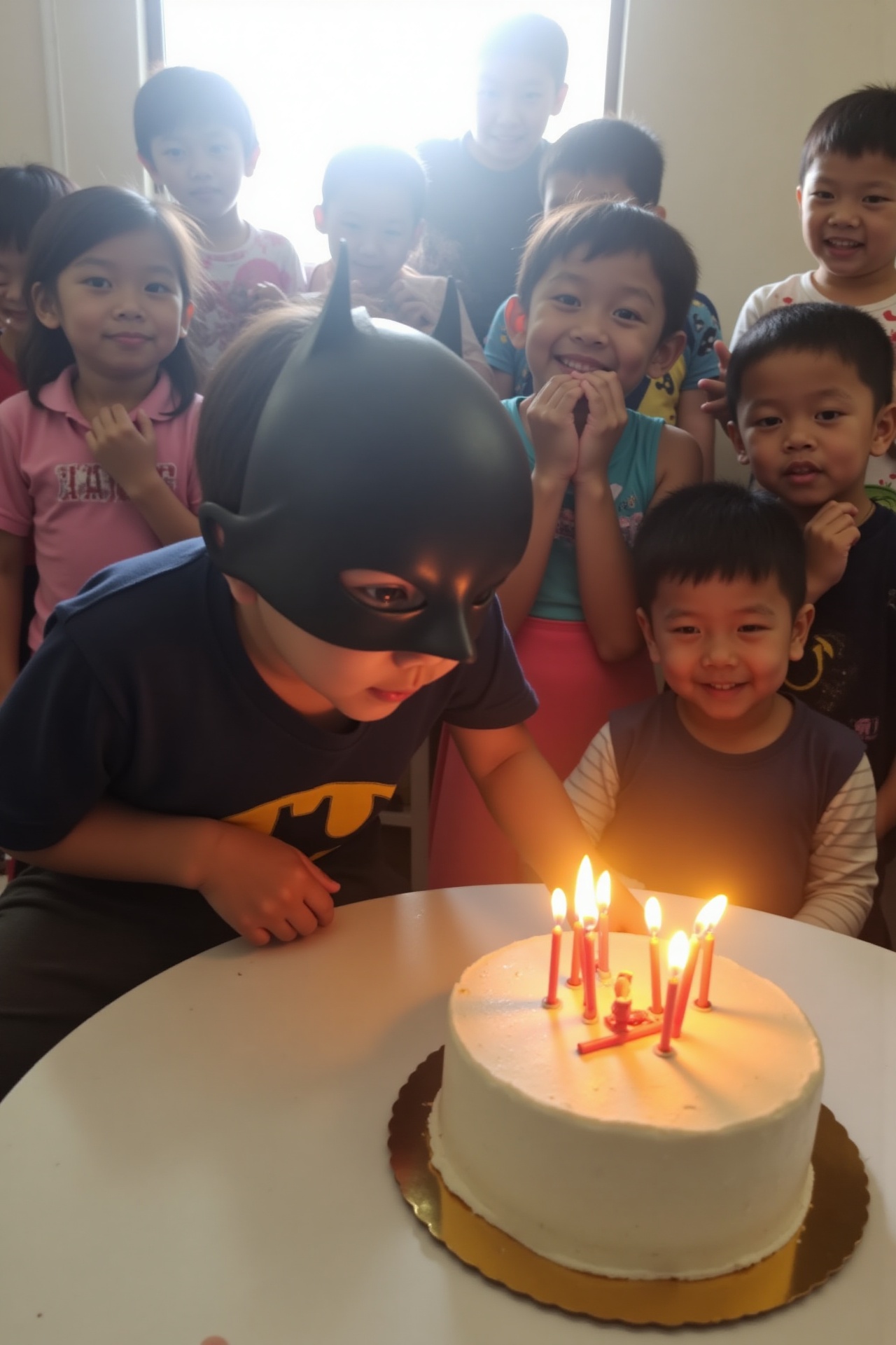 Taken by phone camera,  a small child wearing a Batman mask leans forward to blow out candles on a birthday cake. Natural...