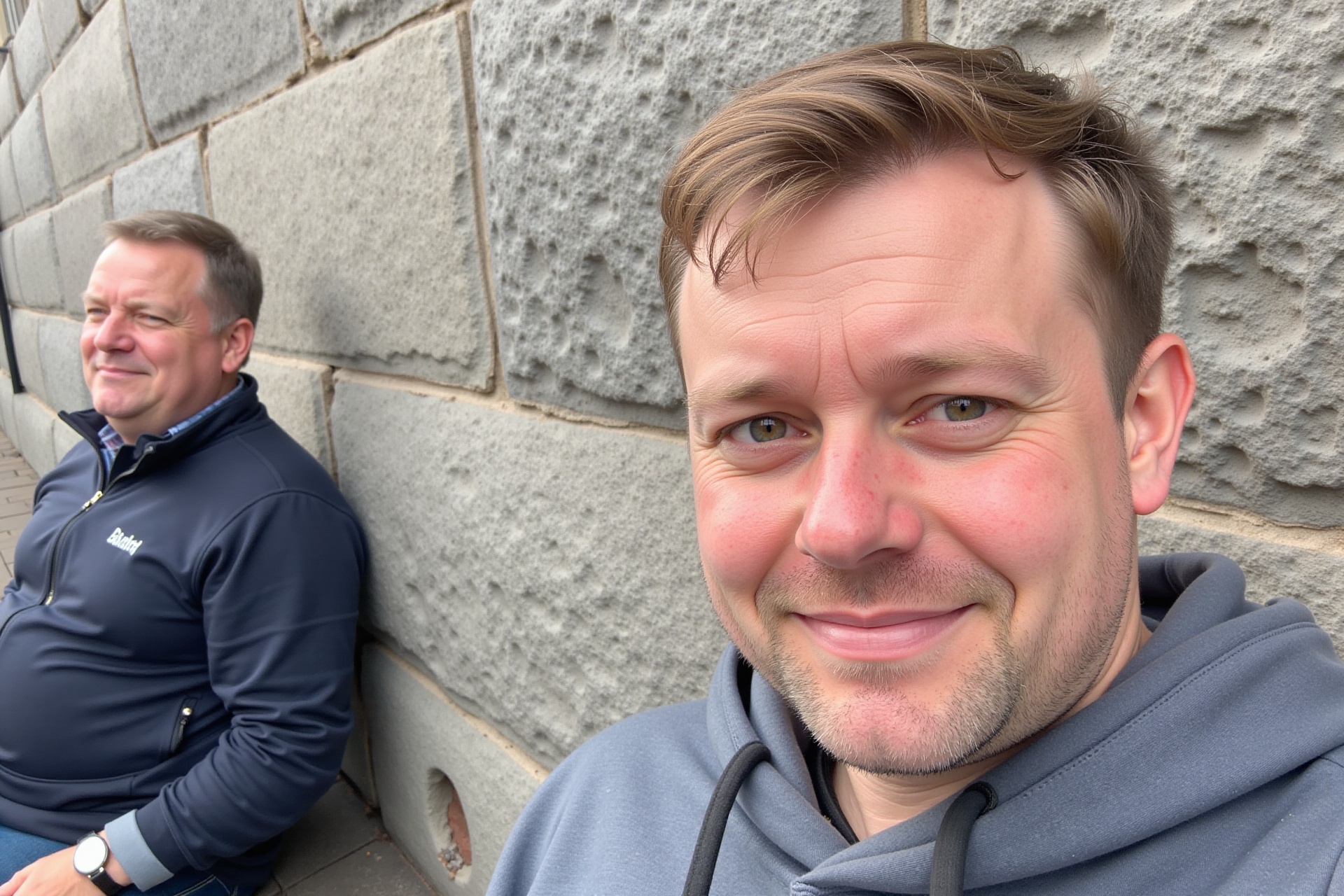 two british men sitting next to a gray stone wall,  one partially seen in a close-up,  eye-level shot on Tensor.Art