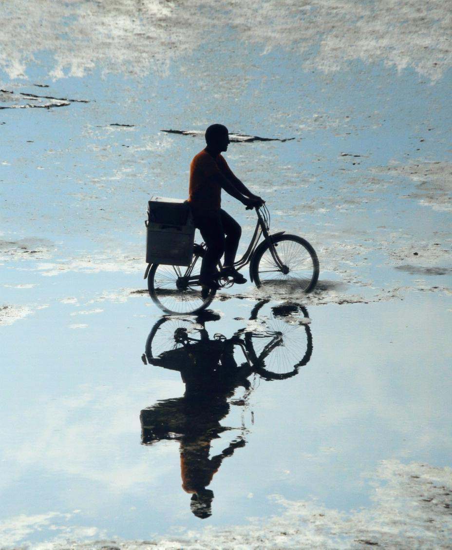 A cinematic photo. A photograph taken from a low angle,  looking up at a silhouette of a person riding a bicycle with a bo...