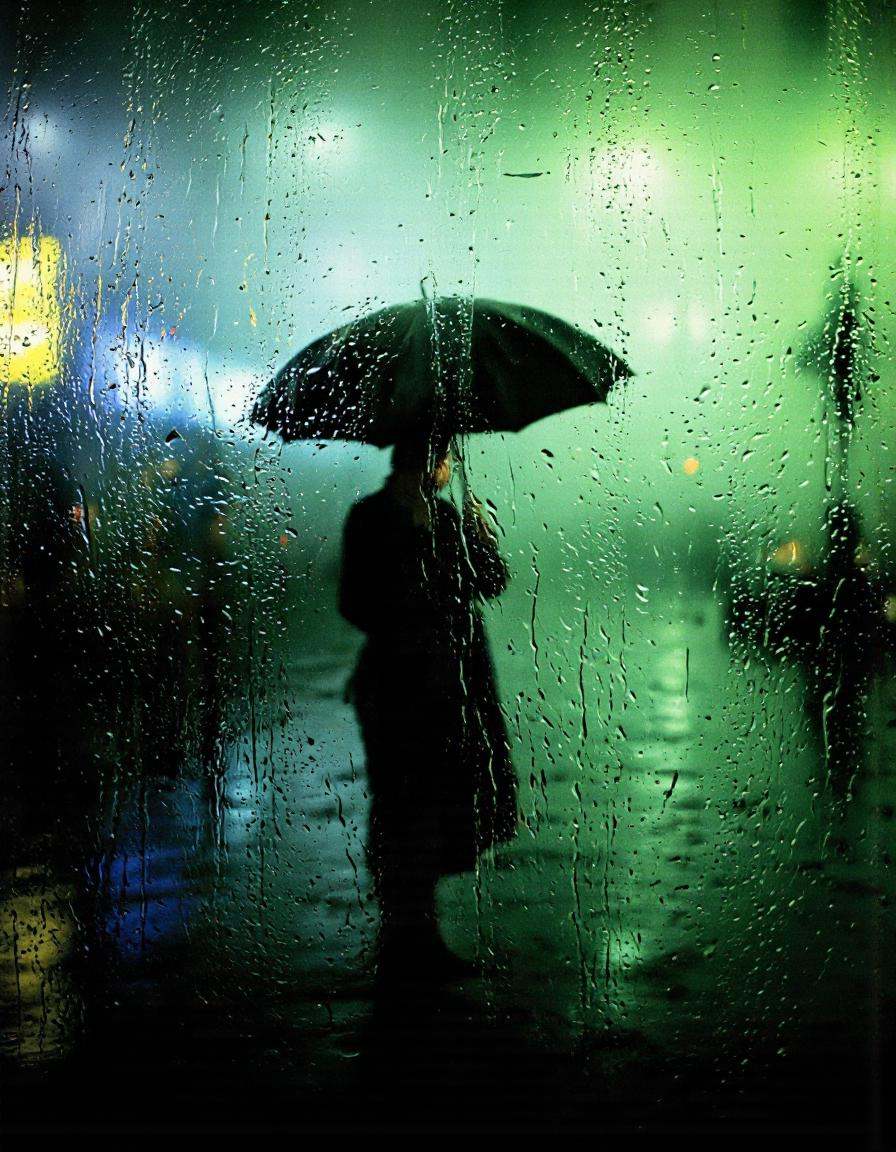 By Saul Leiter. A photograph taken from a low angle,  focusing on a silhouette of a person standing in the rain,  holding...