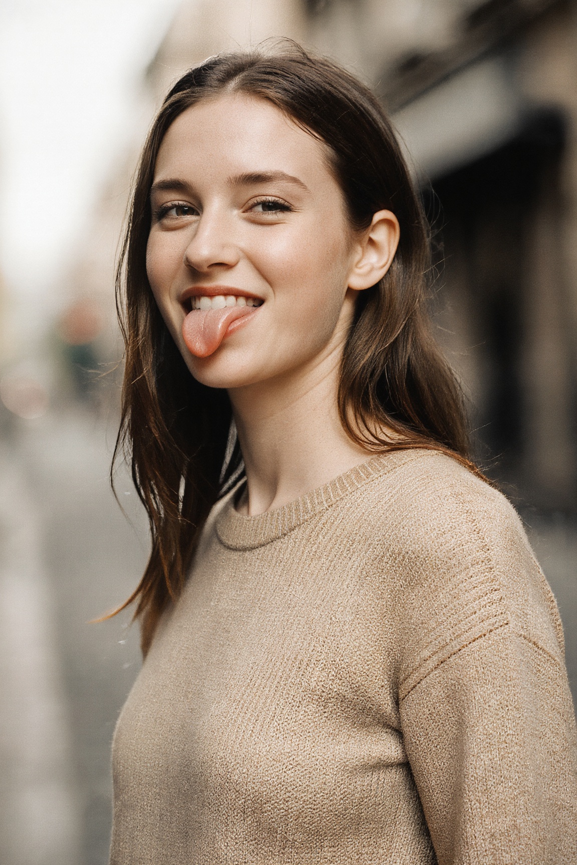 A stylish young woman with slicked-back,  wet-look brown hair,  standing outdoors in an urban setting. She is playfully st...