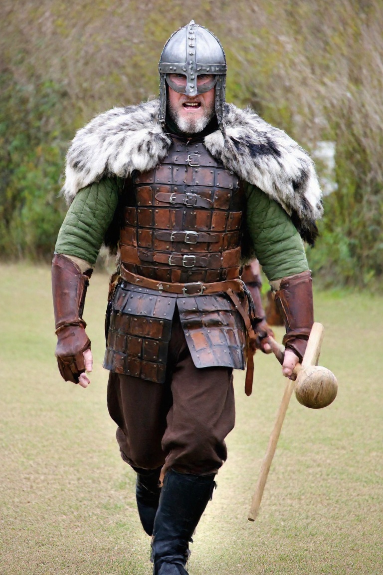 A photograph of a Viking warrior walking toward the camera with his body turned slightly to his left at an outdoor histori...