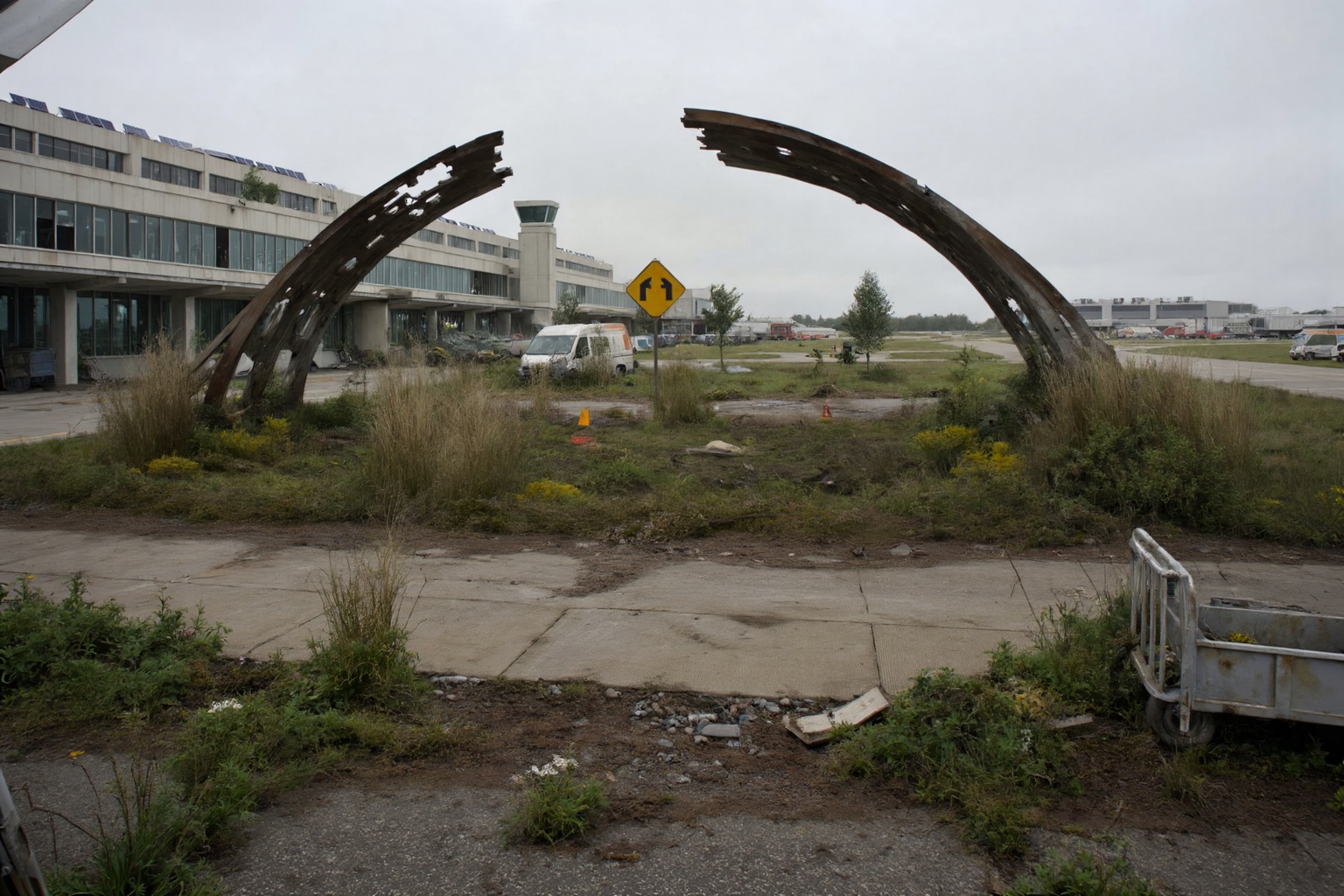 This is a photograph depicting a post-apocalyptic scene of a largely abandoned airport,  functioning as a makeshift settle...