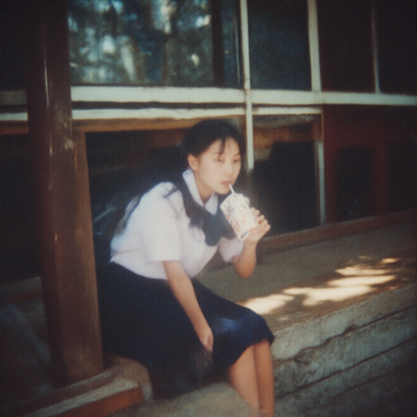 90zVibez ,  A 90s snapshot of a girl in a school uniform sitting on the steps outside a classroom,  drinking juice from a...